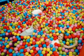 Jouful children lying among many colorful balls in the entertainment center. Girls and boy leisures on holidays, childhood happiness, happy kids on playground