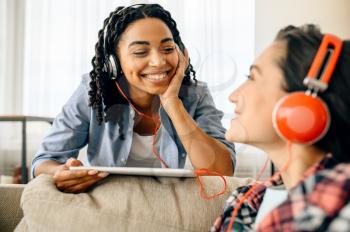 Two happy women enjoys listening to music at home. Pretty girlfriends in earphones relax in the room, sound lovers resting on couch, female friends leisures together
