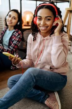 Women in headphones enjoys listening to music at home. Pretty girlfriends in earphones relax in the room, sound lovers resting on couch, female friends leisures together