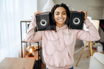 Happy woman holds two audio speakers near her ears and listening to music. Pretty lady relax in the room, female sound lover resting