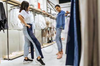 Two girls trying on clothes in clothing store. Women shopping in fashion boutique, shopaholics, shoppers looking garment on hangers