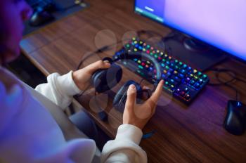 Young gamer holds headphones, gaming club. Virtual entertainment, e-sport championship, cybersport lifestyle. Male person leisures in internet cafe