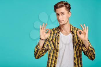 Young man shows Ok sign, blue background, emotion. Face expression, male person looking on camera in studio, emotional concept, positive feelings