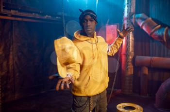 Stylish rapper in yellow hoodie poses in studio with cool underground decoration. Hip-hop performer, rap singer, break-dance