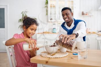 Happy father and daughter having breakfast at home. Smiling family eats on the kitchen in the morning. Dad feeds female child, good relationship