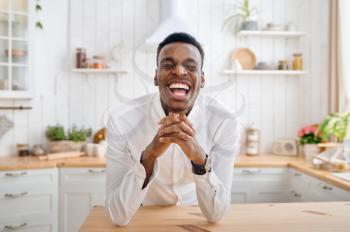 Laughing man sitting at the counter on the kitchen. Cheerful male person poses at the table at home in the morning, happy lifestyle