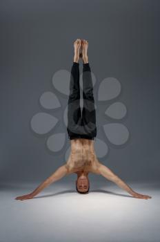 Male yoga standing on his head and hands, meditation, grey background. Strong man doing yogi exercise, asana training, top concentration