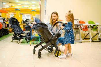 Mother and little daughter choosing baby stroller in store. Mom and adorable girl near the showcase in children's shop, happy childhood, family makes a purchase in kid's market