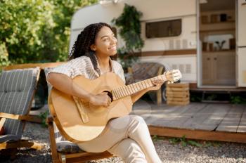 Woman with guitar sitting near the rv, camping in a trailer. Couple travels on van, romantic vacations on motorhome, camper leisures in camping-car, camp
