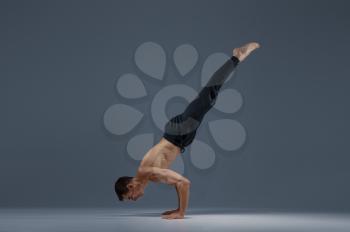 Male yoga keeps balanc on hands, meditation, grey background. Strong man doing yogi exercise, asana training, top concentration, healthy lifestyle