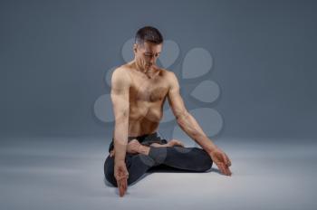 Male yoga maditates in classical pose, meditation position, grey background. Strong man doing yogi exercise, asana training, top concentration, healthy lifestyle