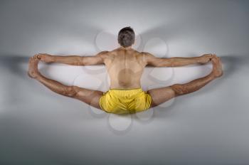 Male yoga sits on a twine, top view, grey background. Strong man doing yogi exercise, asana training, top concentration, healthy lifestyle