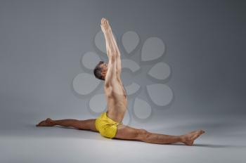 Male yoga sits on a twine, relaxation position, grey background. Strong man doing yogi exercise, asana training, top concentration, healthy lifestyle