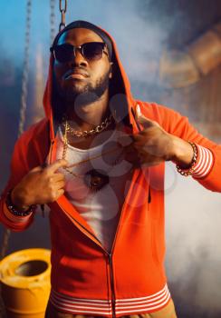 Rapper in red hoodie and sunglasses in studio with cool underground decoration. Hip-hop performer, rap singer, break-dance