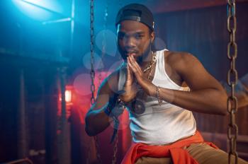 Stylish rapper poses near the chains in studio with cool underground decoration. Hip-hop performer, rap singer, break-dance