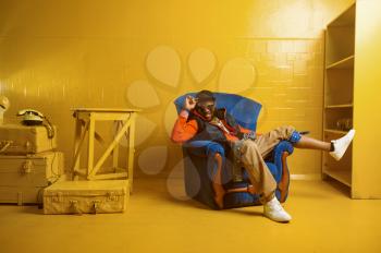 Smiling rapper posing in the chair in studio with yellow tones. Hip-hop performer, rap singer, break-dance performance