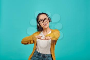 Happy young woman in headphones, blue background, emotion. Face expression, female person looking on camera in studio, emotional concept, positive feelings
