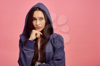 Young thoughtful woman in hoodie, pink background, emotion. Face expression, female person looking on camera in studio, emotional concept, feelings