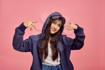 Young smiling woman in hoodie, pink background, emotion. Face expression, female person looking on camera in studio, emotional concept, feelings