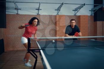 Man and woman play doubles table tennis, ping pong players. Couple playing table-tennis indoors, sport game with racket and ball, active healthy lifestyle