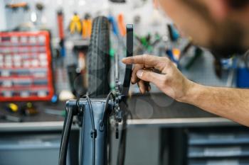 Bicycle assembly in workshop, man setting up a chain. Mechanic in uniform fix problems with cycle, professional bike repairing service