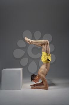Male yoga standing on his elbows, side view, meditation, grey background. Strong man doing yogi exercise, asana training, top concentration, healthy lifestyle