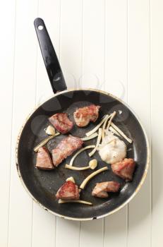 Chunks of pork and garlic on a frying pan