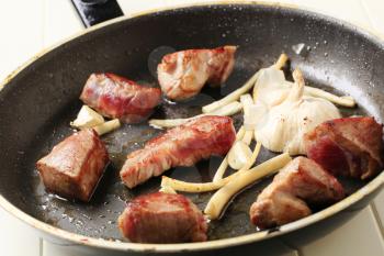 Chunks of pork and garlic on a frying pan