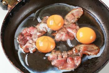 Preparing fried eggs with strips of bacon