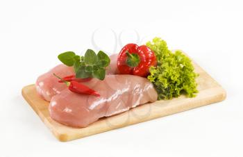 Raw chicken breasts and vegetables on a cutting board