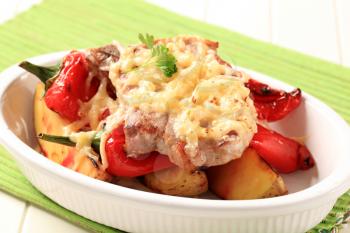 Pork chop topped with grated cheese baked with potatoes and red peppers 
