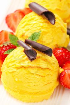 Three scoops of yellow ice cream garnished with chocolate curls and strawberries
