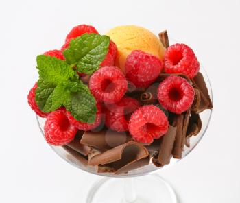 Scoops of ice cream topped with chocolate curls and raspberries