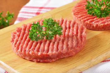 detail of two raw hamburger patties with parsley on wooden cutting board