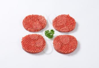 four raw hamburger patties with parsley on white background