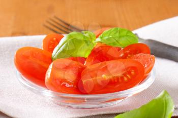 Halved fresh oval-shaped red tomatoes on glass plate