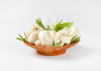 Fresh button mushrooms and culinary herbs in terracotta bowl