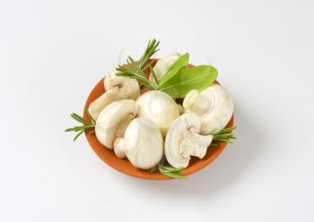 Fresh button mushrooms and culinary herbs in terracotta bowl