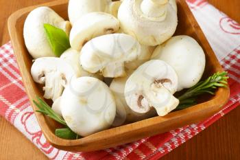 Fresh button mushrooms in square wooden bowl