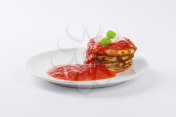 stack of hot pancakes with strawberry puree on white plate