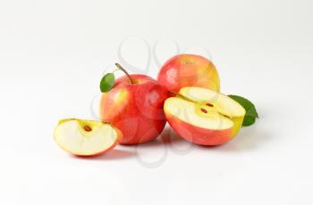 whole and cut apples with leaves on white background