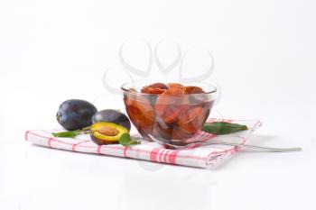Damson compote in a glass bowl and fresh plums next to it on checked dishcloth