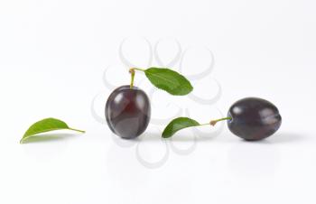 two ripe plums with leaves on white background