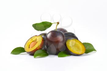 whole and halved plums on white background