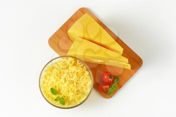 bowl of grated cheese and two wedges of cheese on wooden cutting board