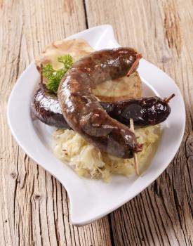 Blood sausage and white pudding with sauerkraut and baked potato on wooden background