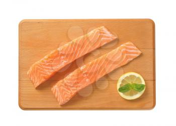 two raw salmon fillets on wooden cutting board