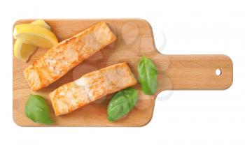 two cooked salmon fillets on wooden cutting board
