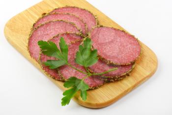 slices of green pepper coated salami on wooden cutting board