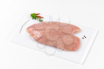 raw turkey breast fillets on white plastic cutting board